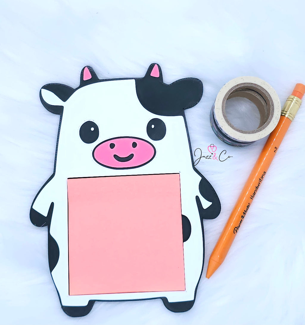 Cow-shaped notepad with a pink center, surrounded by tape and a pencil on a white background